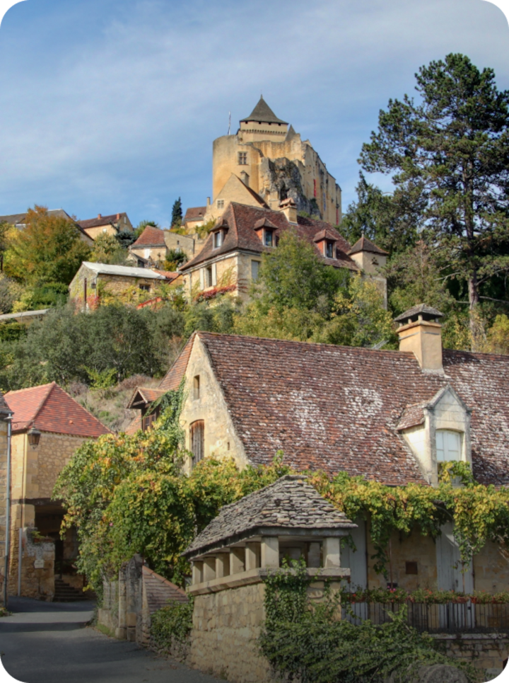 Un village pittoresque avec des maisons en pierre à flanc de colline, traversé par une route étroite. Texte superposé : « Étape 8 Périgueux », avec une flèche vers la droite.