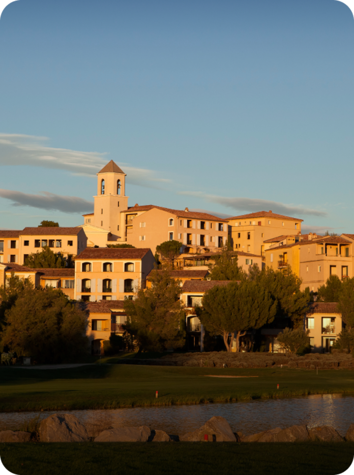 Un village à flanc de colline au coucher du soleil, avec des bâtiments aux teintes pastel et son clocher. Texte superposé : « Étape 9 Malemort », avec une flèche vers la droite.