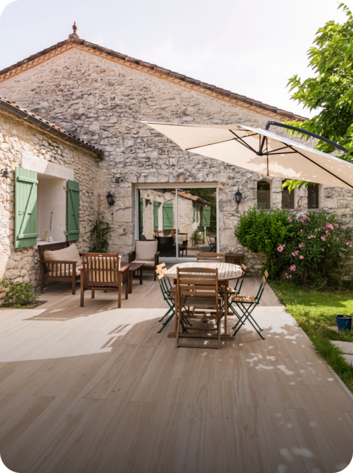 Une terrasse ensoleillée dans un jardin à Aurillac, avec la mention « Étape 10 Aurillac » en bas à gauche et une flèche vers la droite.