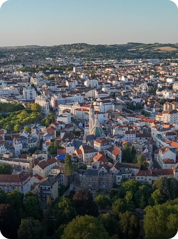 Vue aérienne de Vichy, où se mêlent des toits rouges et des bâtiments blancs, dans un écrin verdoyant d'arbres et de parcs. Texte superposé : « Étape 11 Vichy », avec une flèche vers la droite.