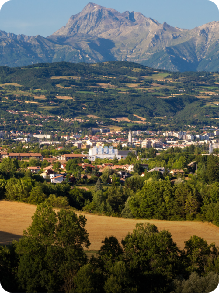 Vue panoramique de Gap entourée de champs et de forêts verdoyants. Texte superposé : « Étape 19 Gap », avec une flèche vers la droite.
