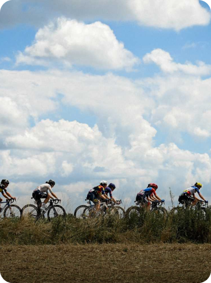 Des cyclistes professionnels roulent en peloton sur une route de campagne sous un ciel bleu éclatant. Texte superposé : « Étape 6 Montbrison », avec une flèche vers la droite.