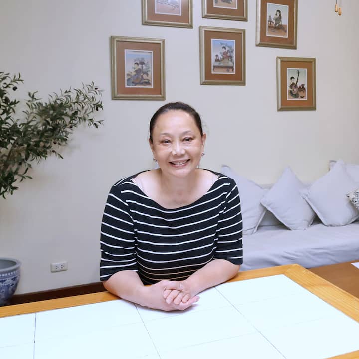 Host sitting at a table in a bright SEA home, with framed art and cushions in the background
