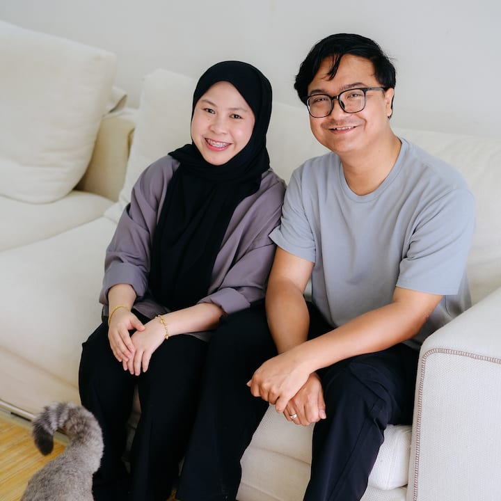 airbnb.org hosts sitting together on a white couch in a bright living room with a small gray cat nearby.