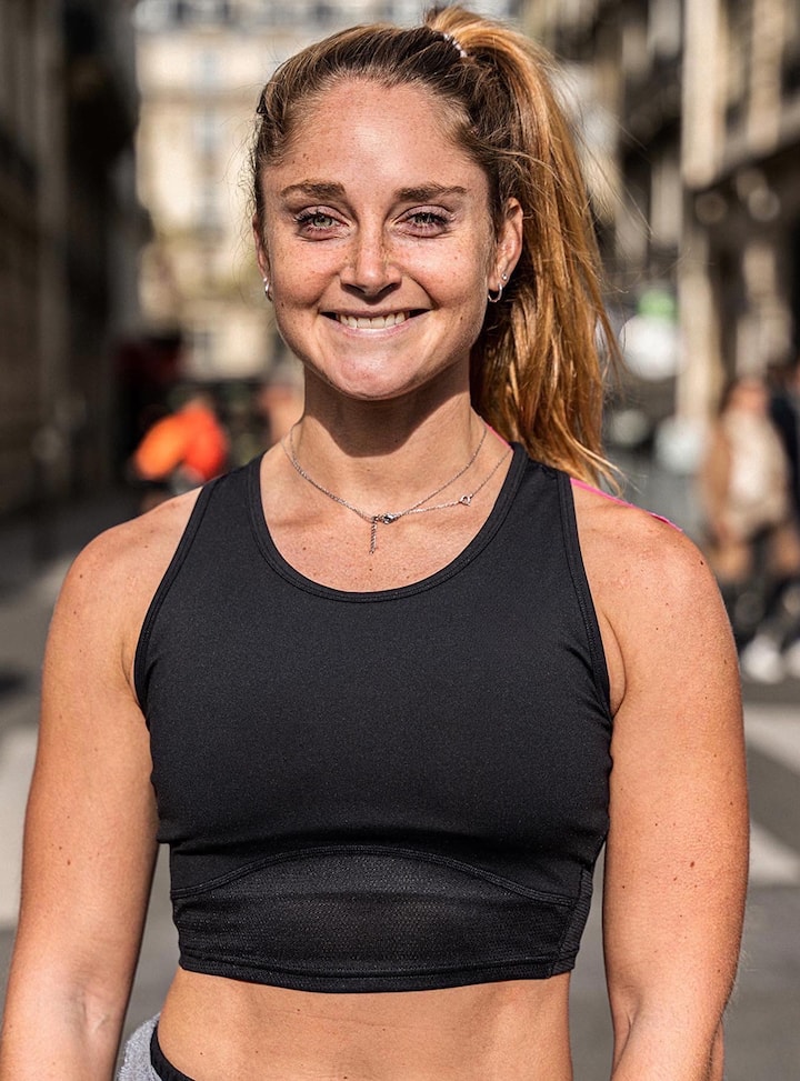Une coureuse vêtue d'un haut de sport noir se tient debout dans une rue parisienne ensoleillée