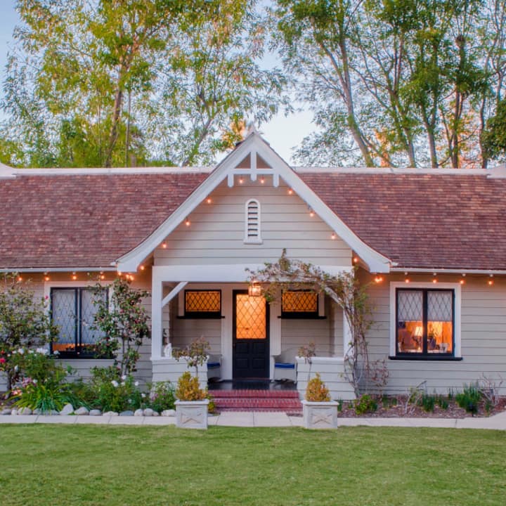 Une charmante maison aux allures de cottage, dotée d'un toit à pignon et d'une pelouse bien entretenue à l'avant, entourée d'arbres.