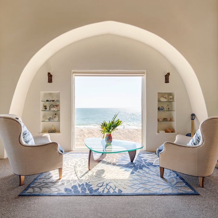 Un coin salon chaleureux avec des fauteuils et une table basse en verre, installé devant une grande baie vitrée donnant sur la plage.