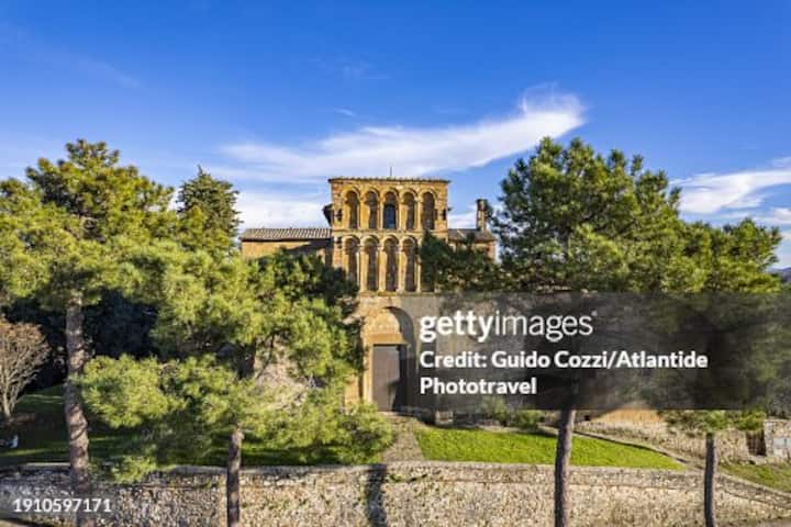 Storico borgo italiano immerso nel verde, con chiesa in pietra tra gli alberi, a rappresentare i piccoli comuni rurali Airbnb.