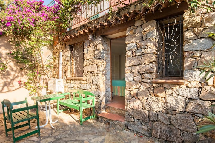 Sunny stone cottage with small patio table and green chairs, suggesting dispersed rural tourism stay.
