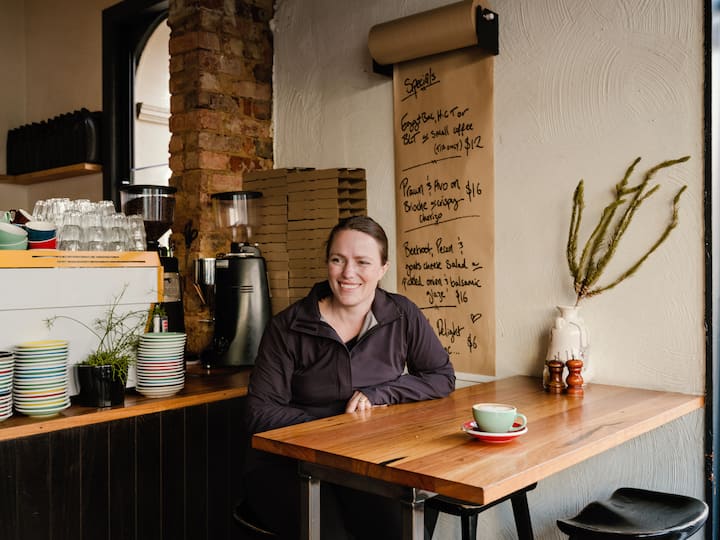 Host sits at a small café table with a coffee, suggesting everyday Australians using Airbnb homes in strata communities