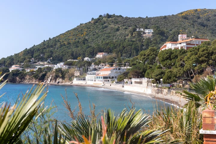 Piccolo borgo costiero italiano con case affacciate sul mare e colline verdi, simbolo di turismo rurale tramite Airbnb