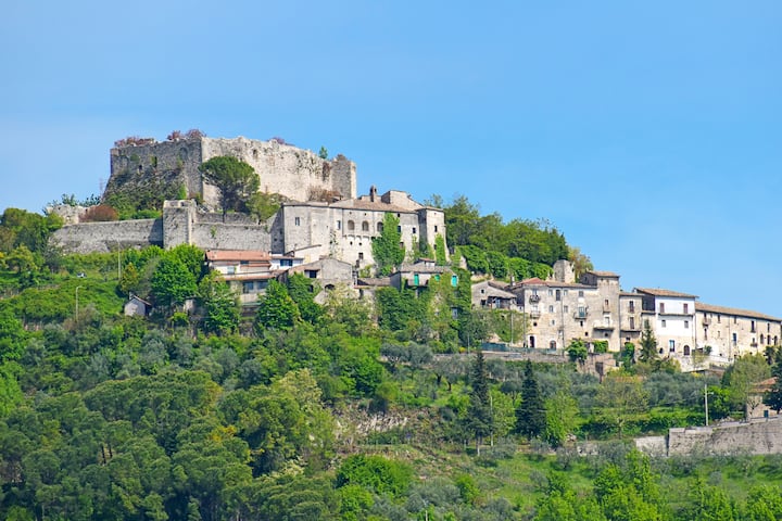 Borgo rurale italiano su una collina verde, con case in pietra e un castello storico, accessibile solo tramite Airbnb