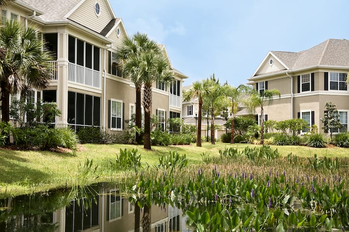 A photo of a housing complex in Florida, with palm trees and a pond in the foreground.