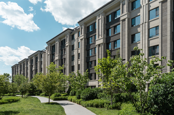 A photo of a modern housing complex bordered by a green space with walking path.