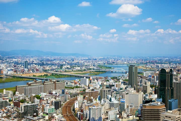 高層ビルと住宅が立ち並ぶ都市と、大きな川と橋を見渡す昼間のパノラマ風景。