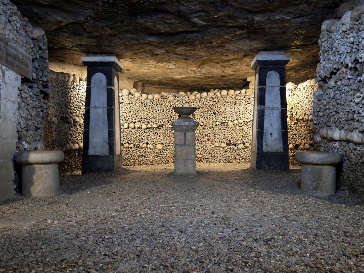 Underground chamber in the Paris Catacombs lined with stacked skulls and bones around stone pillars