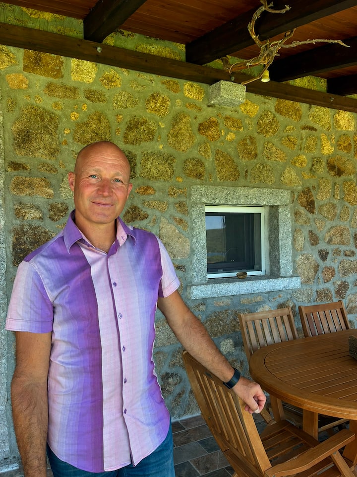 Host standing on the stone terrace of Stazzu Iris in Calangianus, next to a wooden outdoor dining table