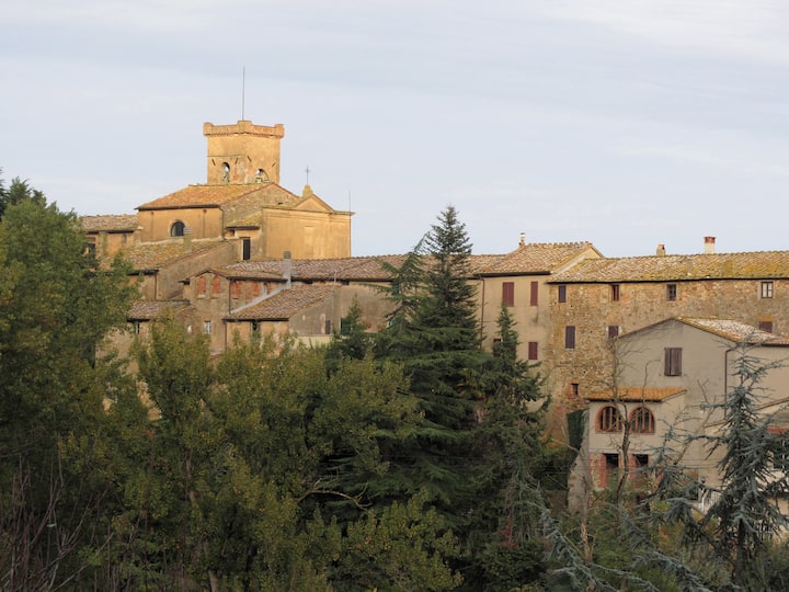 Borgo collinare italiano con case in pietra e campanile, immerso nel verde, simbolo di piccoli comuni senza hotel.