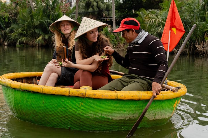 Guests ride in a round green boat on a Vietnamese river led by a local guide with a red flag.