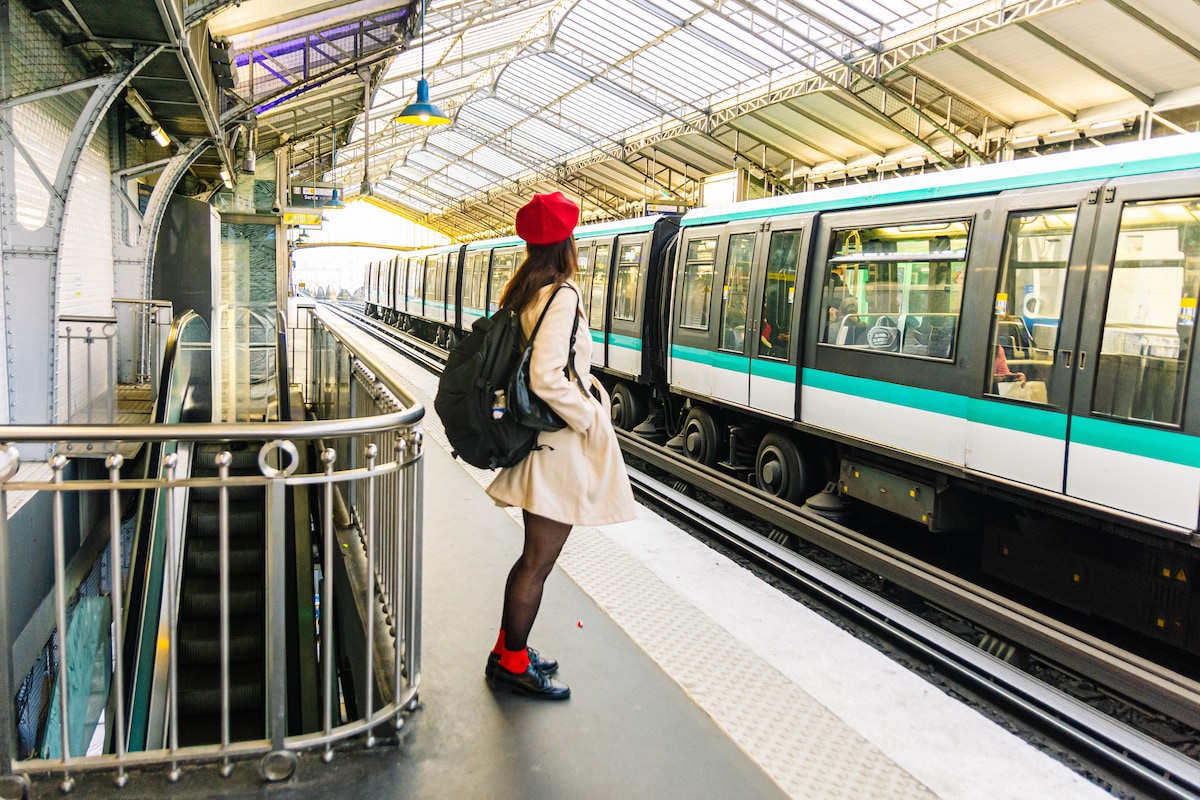 Solo traveler in a red beret waits on a Paris Metro platform, ready to explore the city independently.