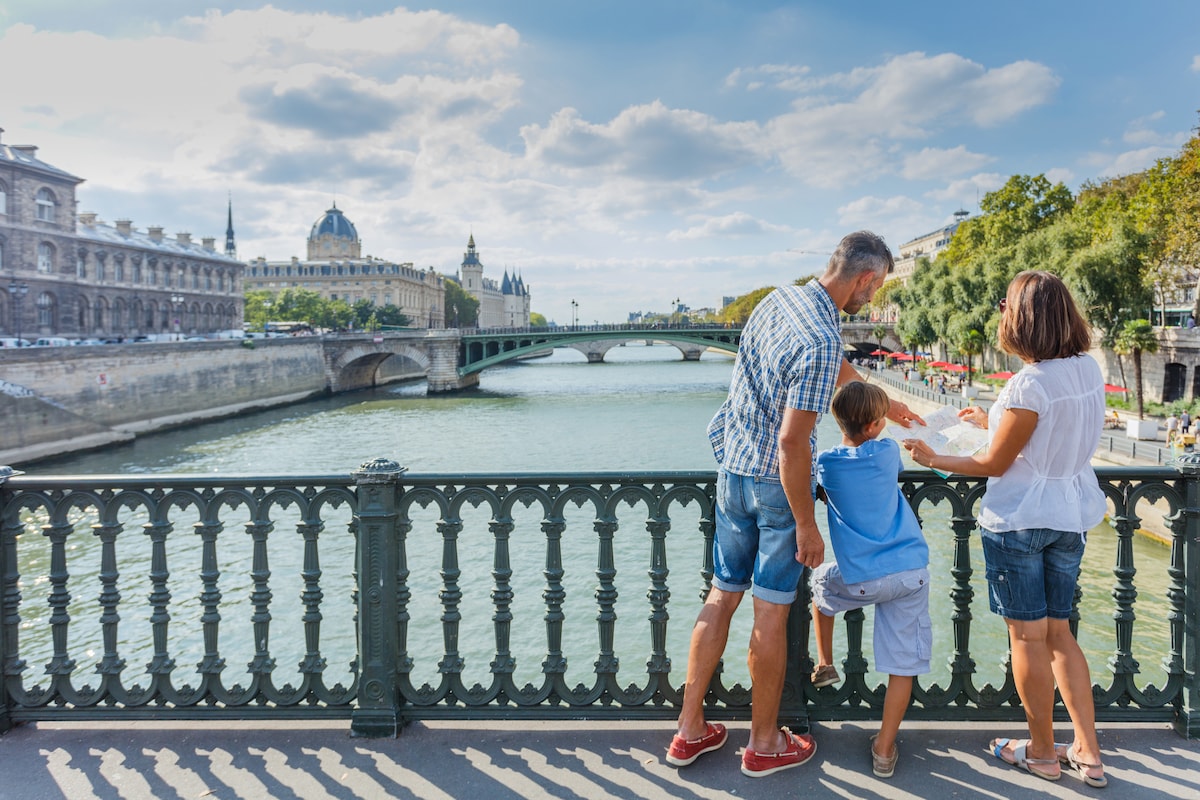 Parents and child pause on a bridge above the Seine, enjoying Paris together in the sunshine