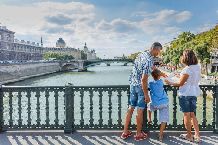 Parents and child pause on a bridge above the Seine, enjoying Paris together in the sunshine