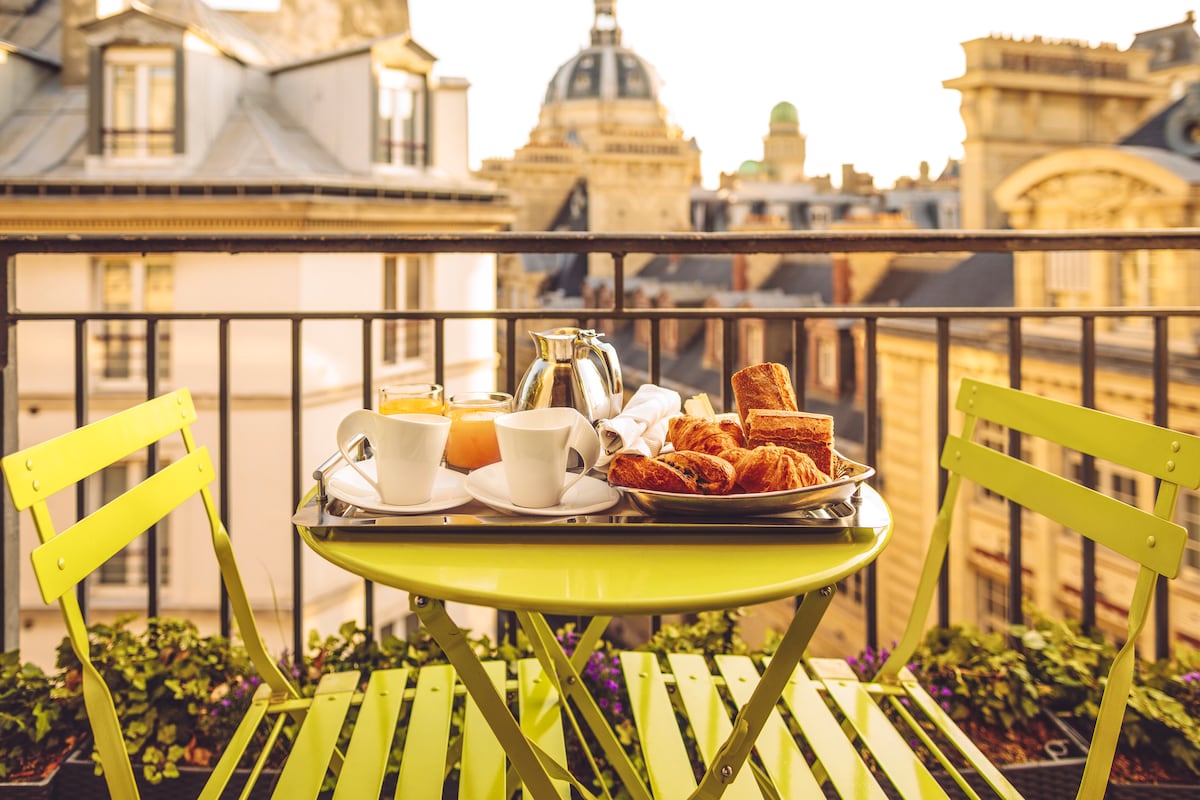 Breakfast of croissants and coffee on a balcony table overlooking Parisian rooftops and domes