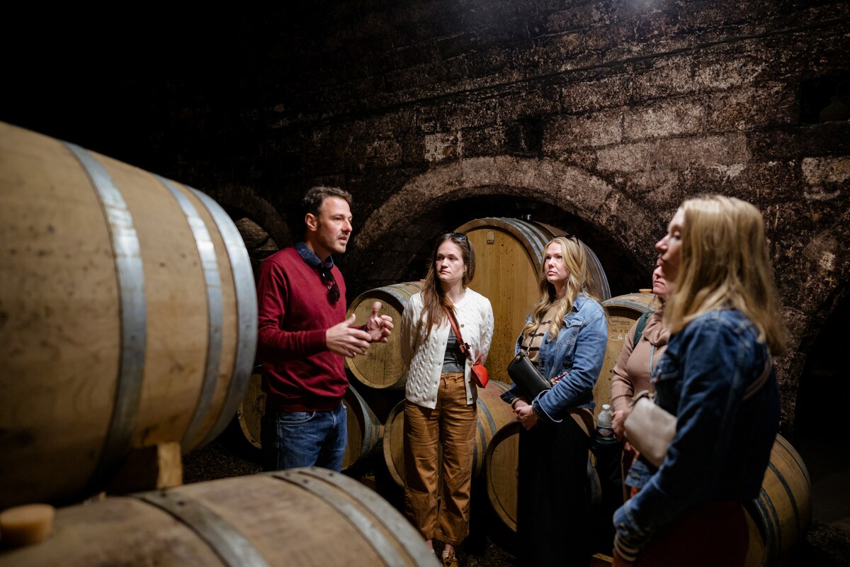 Group of travelers on a guided wine cellar tour surrounded by large wooden barrels