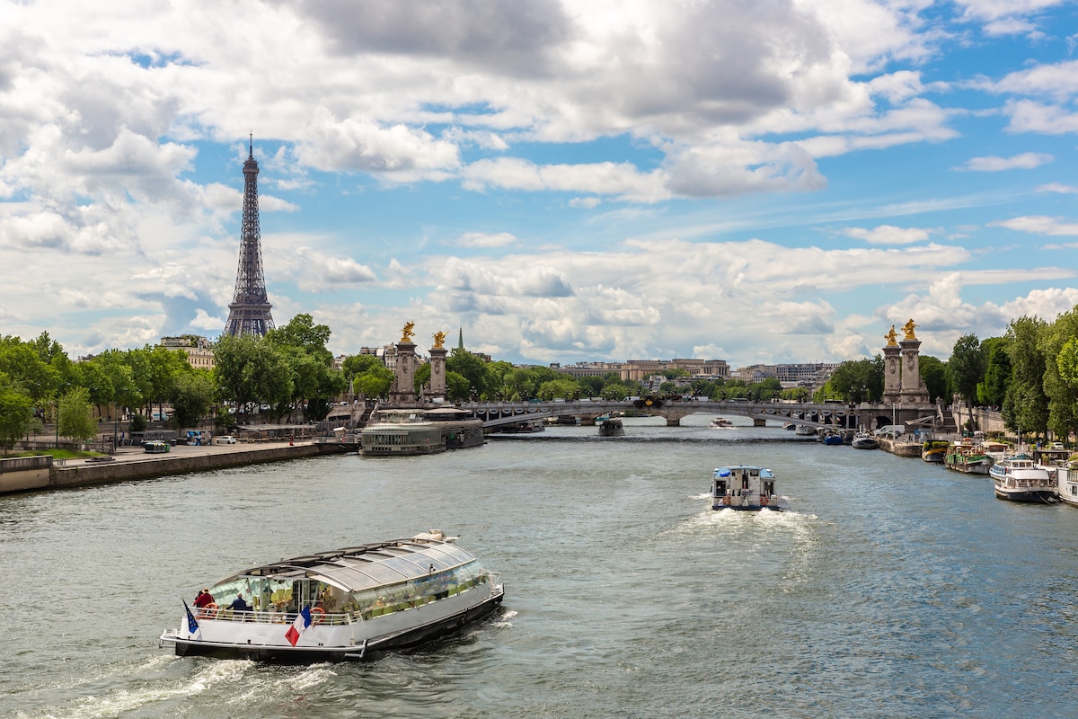 Boats cruising the Seine in Paris with the Eiffel Tower and city bridges in view under a bright sky.