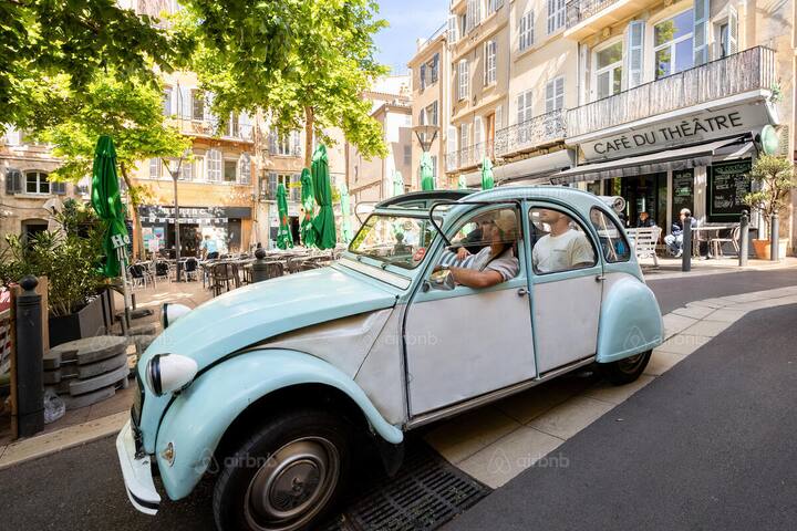 Small group riding in a vintage car past a café, on a guided city tour through a European square
