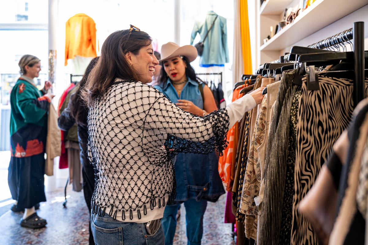 Guests browse colorful racks of vintage clothing in a Paris boutique during a shopping experience.