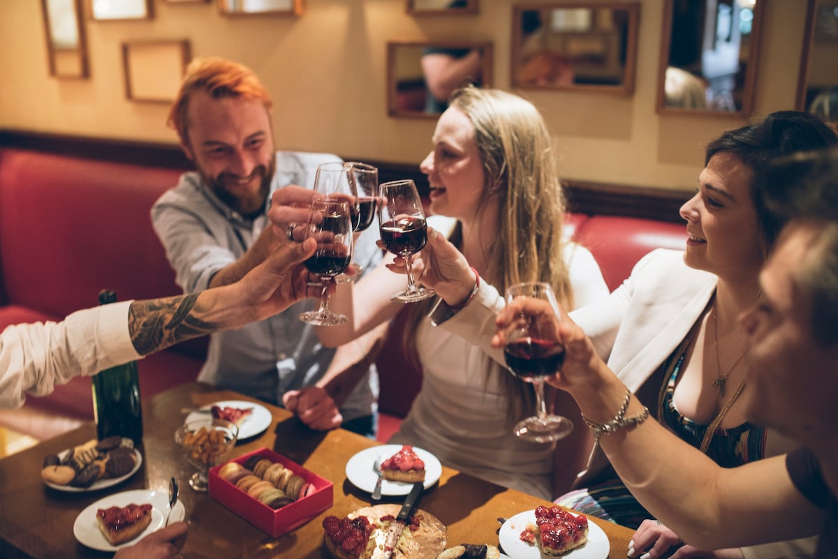 Friends raise glasses of red wine over pastries in a cozy Paris bar during a nightlife experience.