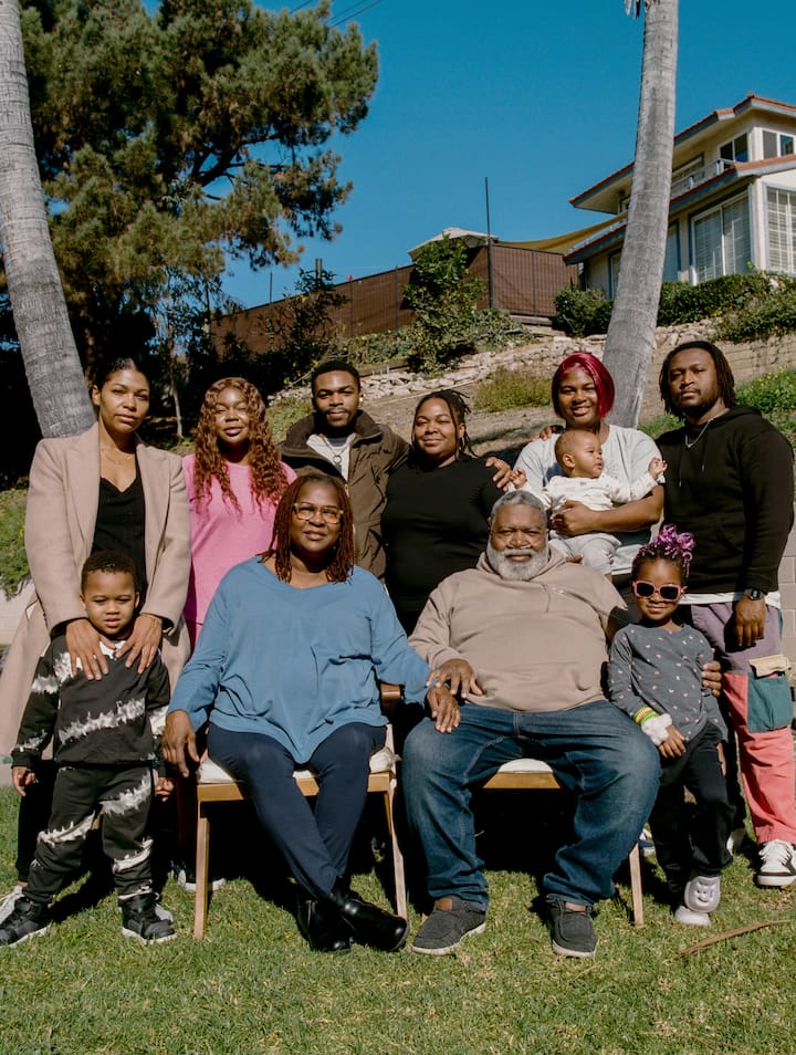 A large multigenerational family gathered together on a lawn in front of a home on a sunny day.