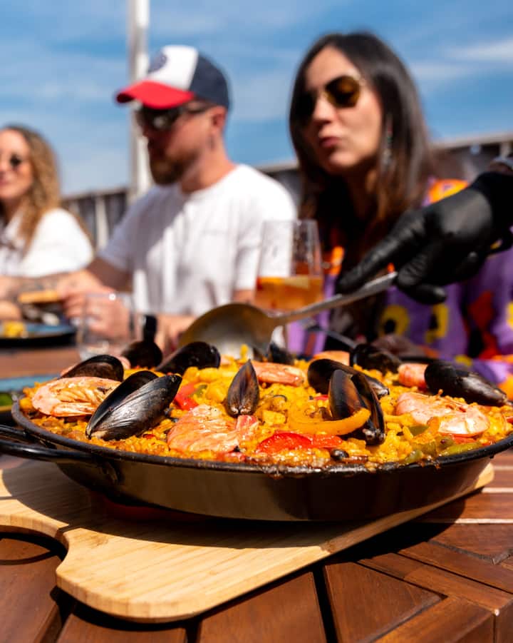 Unos amigos comparten una paella de marisco al aire libre en Barcelona durante una experiencia centrada en el eclipse.