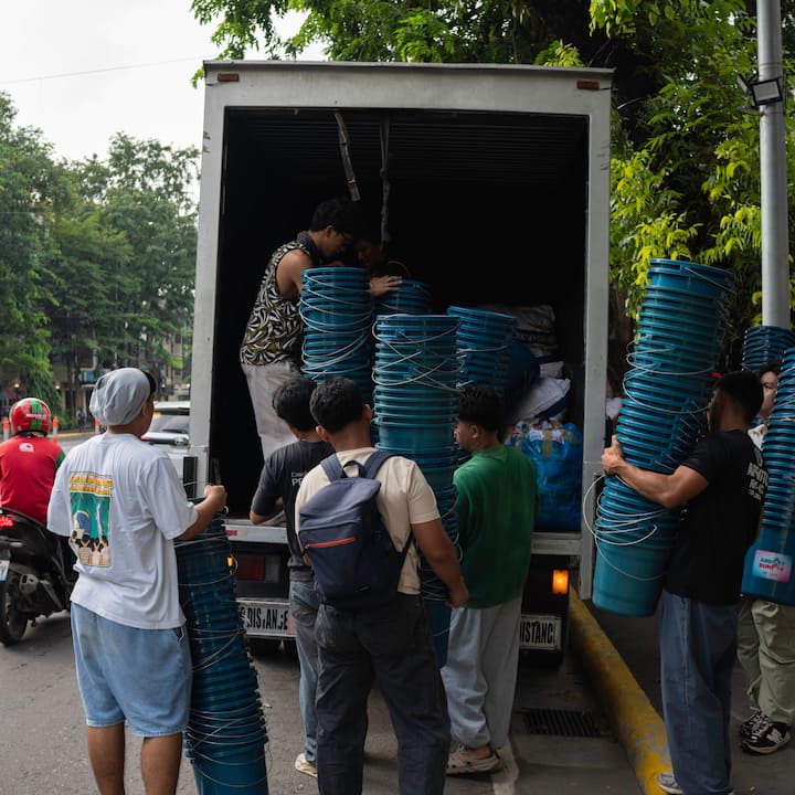 Sekumpulan orang memunggah baldi dari belakang lori yang terletak di atas jalan yang dibarisi dengan pokok.