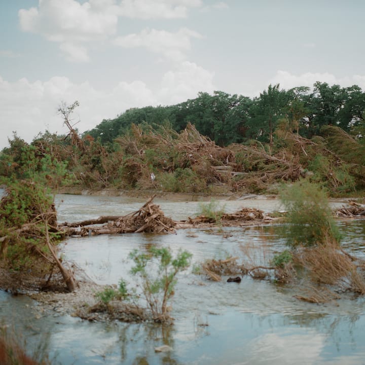 Lanskap yang dilanda banjir dengan pokok-pokok tumbang dan serpihan yang dibawa oleh air banjir berlumpur.