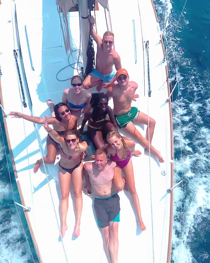 Un grupo de viajeros sonríen a la cámara en un velero en el Mediterráneo. La imagen representa las experiencias relacionadas con el eclipse en Barcelona.