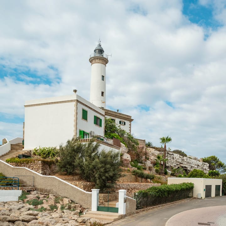 Un faro en lo alto de un acantilado con una casa blanca adosada que tiene vistas a una sinuosa carretera costera en Mallorca, en las islas Baleares.