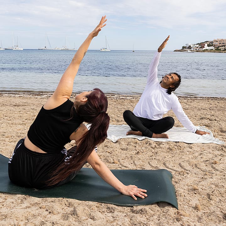 Una sesión de yoga en la playa junto a la costa de España desde la que se verá el eclipse. Dos viajeros estiran el brazo hacia el cielo con el mar a sus espaldas.