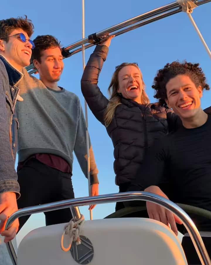 Un grupo de amigos en la cubierta de un barco iluminada por el sol sonríe mientras navega para disfrutar de una experiencia sobre el eclipse en las islas Baleares.