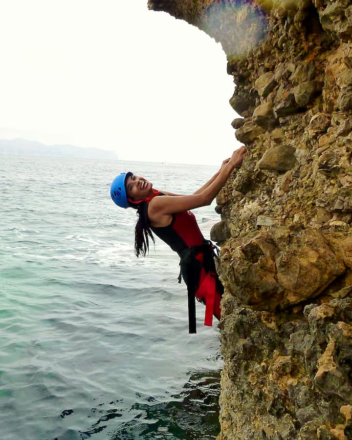 Una mujer aventurera escala un acantilado costero sobre el Mediterráneo. La imagen representa escapadas activas relacionadas con el eclipse en Mallorca, Ibiza o Menorca.