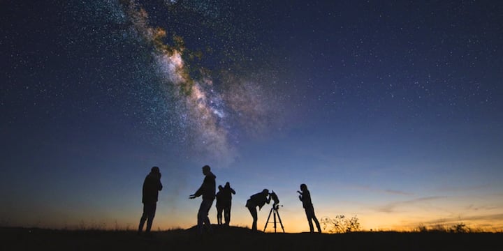 Las siluetas de unos viajeros que utilizan telescopios para observar el cielo nocturno. La imagen promociona las estancias en Airbnb relacionadas con el eclipse y la astronomía.