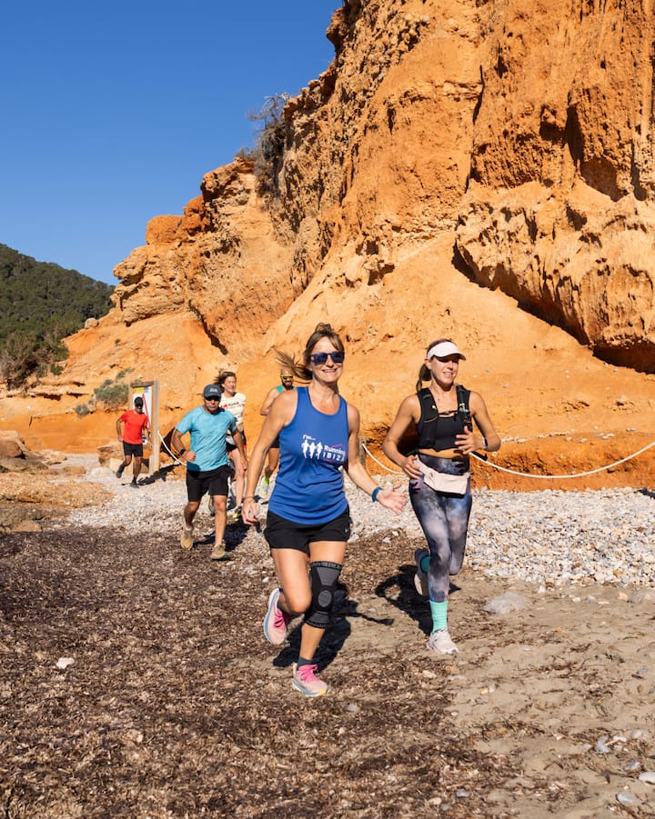 Varias personas corren a lo largo de una playa rocosa bajo acantilados de color naranja intenso. La imagen muestra una escapada activa para ver el eclipse.