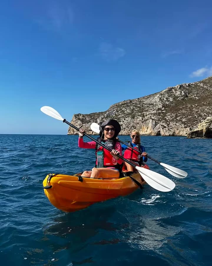 Dos personas en kayak en aguas turquesas cerca de los acantilados de Valencia, disfrutando de la experiencia del eclipse en la costa.