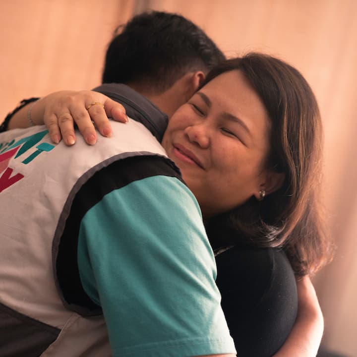 A woman embraces a relief worker in a tight, emotional hug, smiling with her eyes closed.