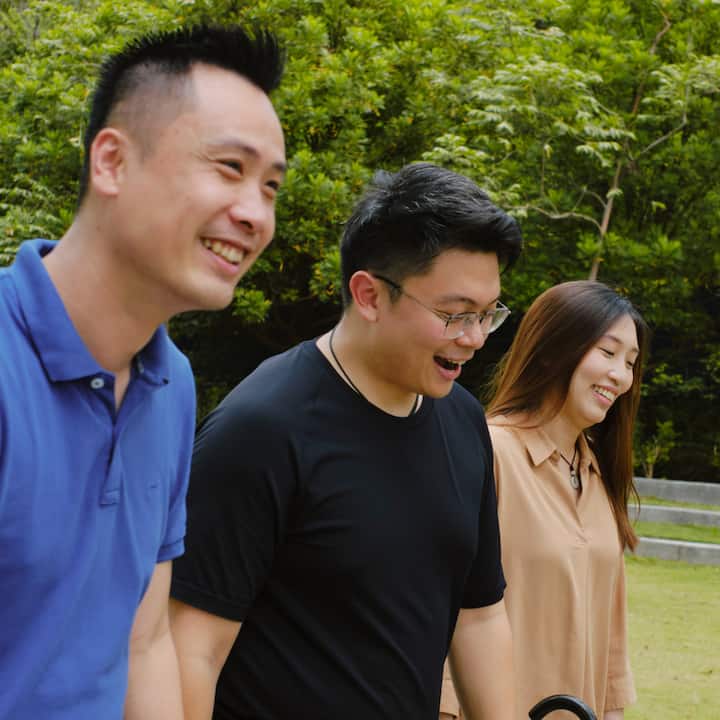 Three people walking together outdoors, smiling, with greenery in the background.