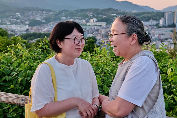 Smiling Seongbuk-dong host chatting with a guest on a hilltop overlooking the neighborhood at sunset
