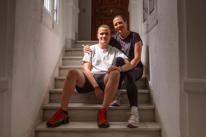 Žena i njezin sin sjede jedno pored drugoga na stepenicama koje vode do smještaja koji su dobili putem Airbnba i smiješe se gledajući u kameru.