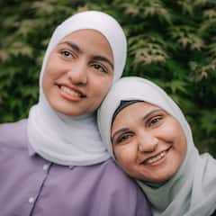 Dalawang babae na parehong nakasuot ng hijab ang magkasamang nakangiti sa labas.