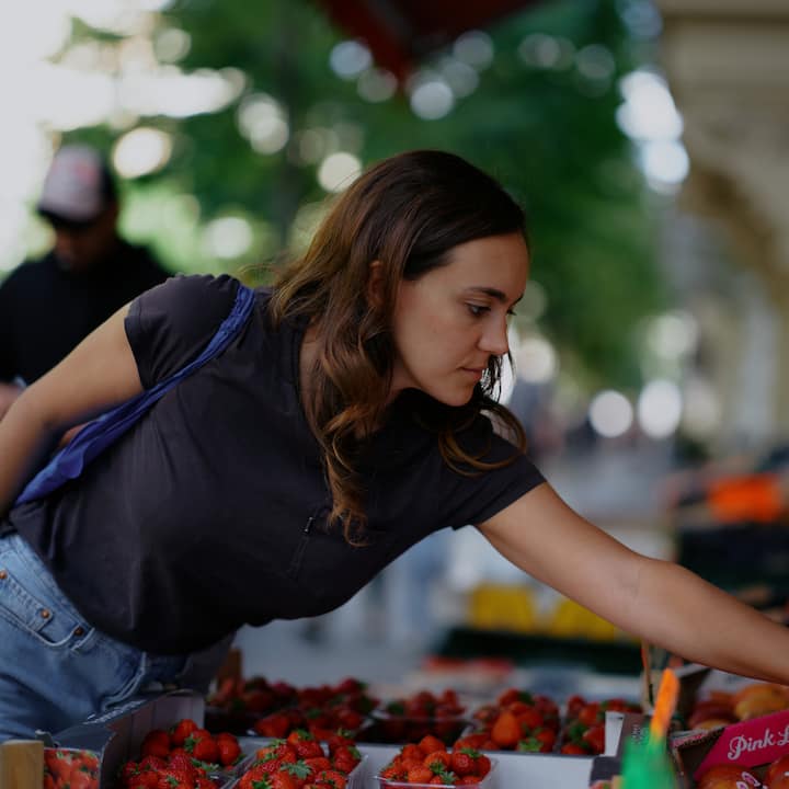 A woman reaching over a display of strawberries at an outdoor market.